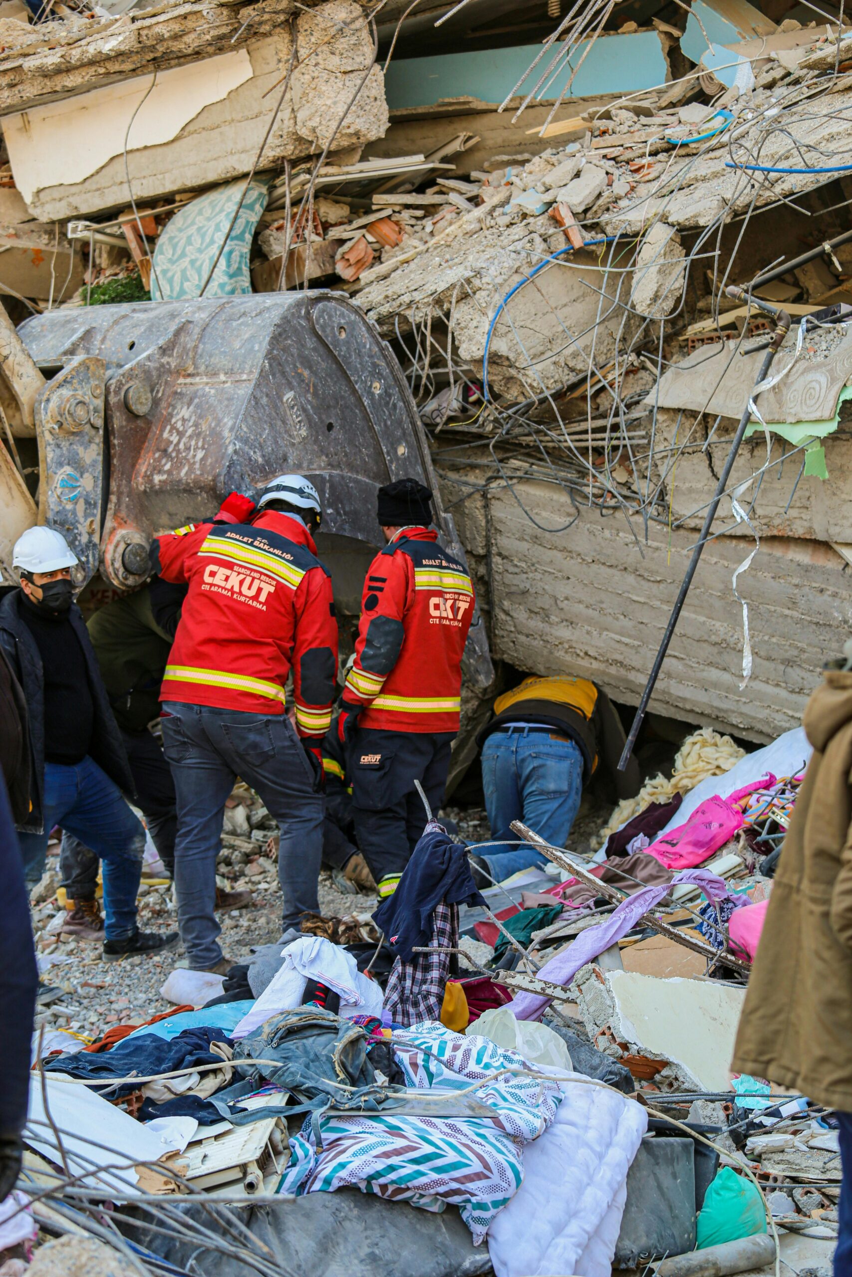 Rescue workers in red uniforms search through the rubble of a collapsed building after an earthquake.